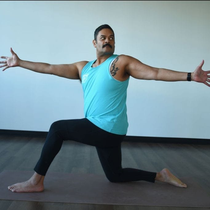 Ganesh Sharma practices ahimsa and kindness in a revolved low lunge at Myriad Yoga